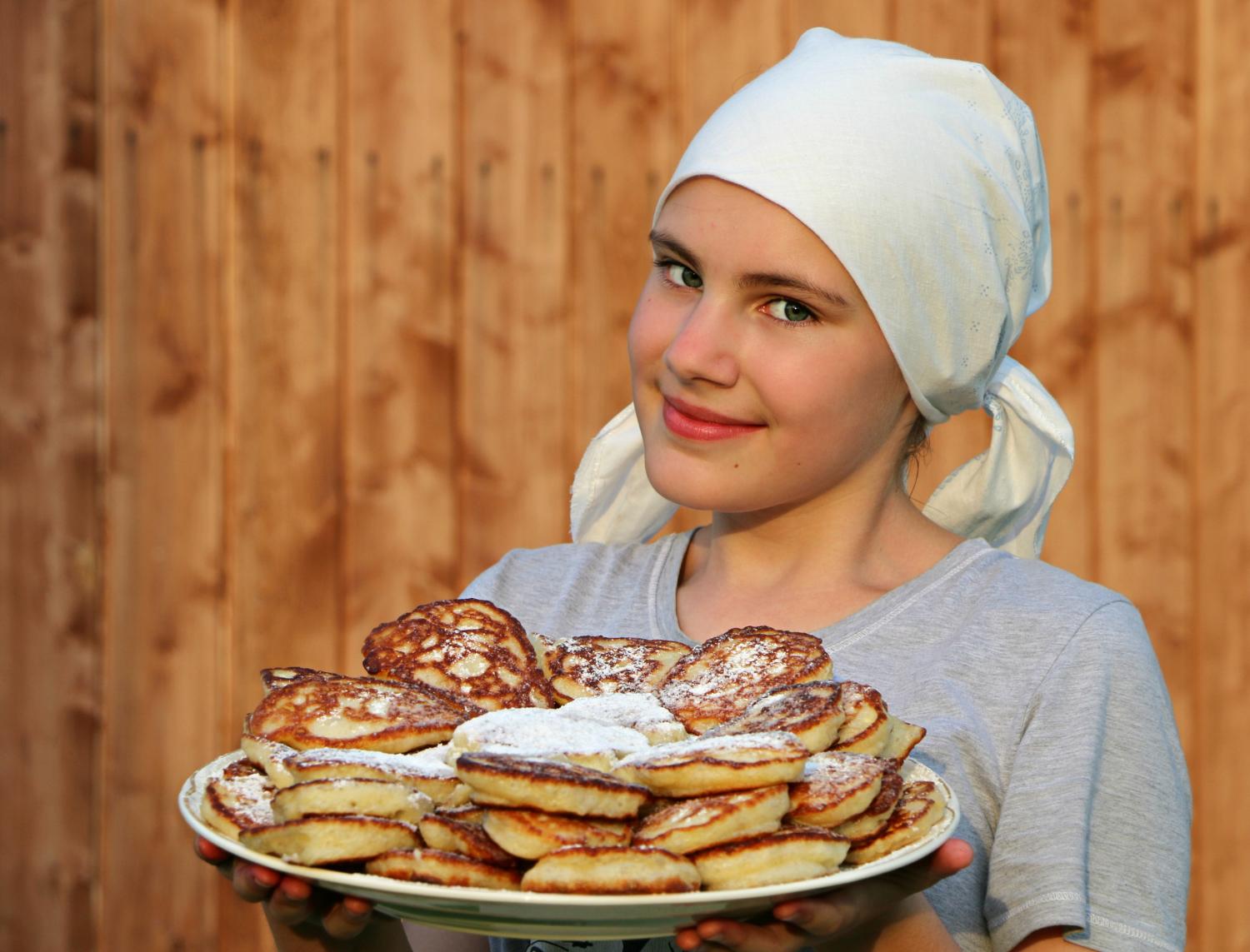 Tytöllä valkoinen huivi, kädessä pannukakkulautanen