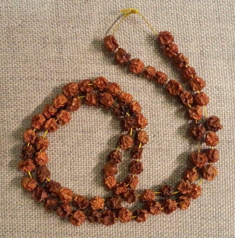 Pihlajanmarjoista tehty käsintehty kaulanauha, jossa kuivuneet, ruskeiksi muuttuneet marjat on pujotettu tiheästi keltaiseen lankaan. Nauha on aseteltu kevyelle kaarelle vaaleanharmaata, karkeapintaista kangasta vasten.